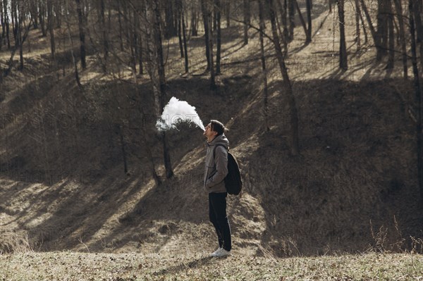 Middle Eastern man blowing vapor from mouth in forest