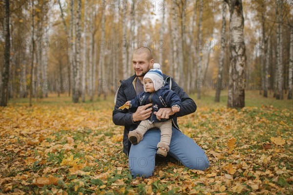 Middle Eastern father kneeling in park with baby son in autumn