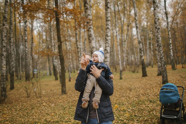 Middle Eastern father holding baby son and pointing in autumn