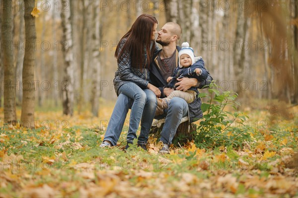 Middle Eastern couple sitting on tree stump with baby son in autumn