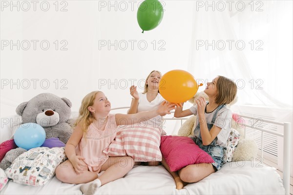 Middle Eastern sisters sitting on bed playing with balloons