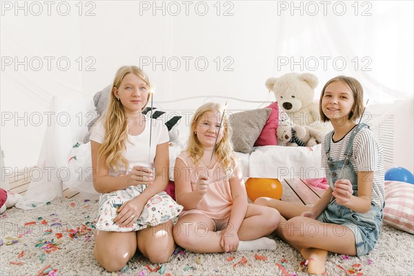 Portrait of smiling Middle Eastern sisters holding sparklers in bedroom