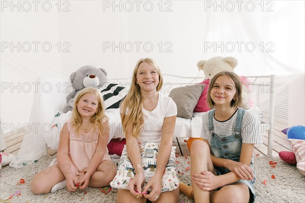 Portrait of smiling Middle Eastern sisters sitting on floor in bedroom