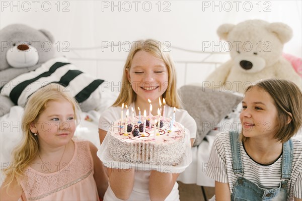 Smiling Middle Eastern sisters with birthday cake in bedroom