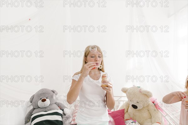 Middle Eastern girl blowing bubbles in bedroom