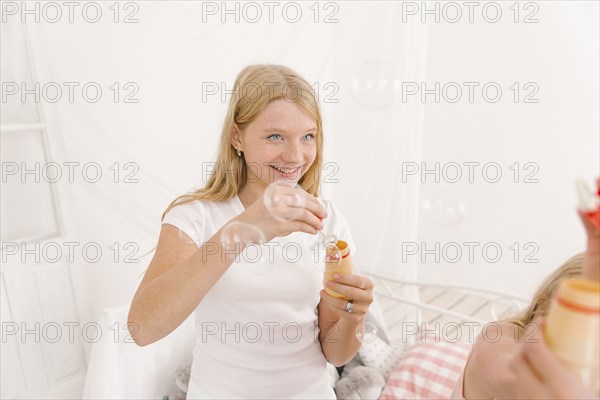 Middle Eastern girl blowing bubbles in bedroom