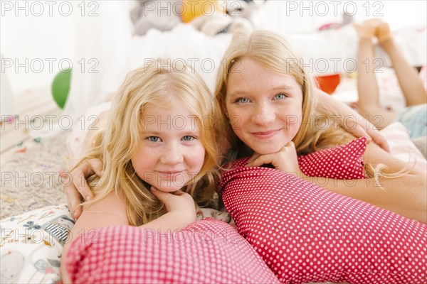 Portrait of smiling Middle Eastern sisters laying on floor