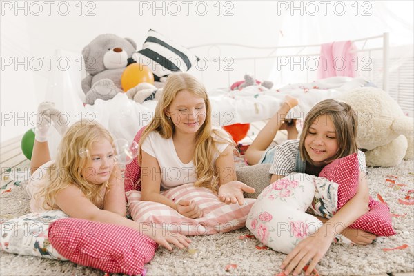 Smiling Middle Eastern girls laying on floor watching bubbles