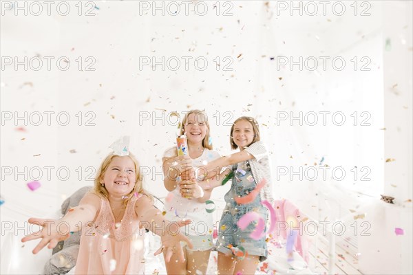 Smiling Middle Eastern girls throwing confetti in bedroom