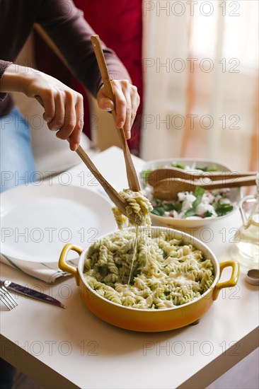 Woman serving pasta with wooden spoons