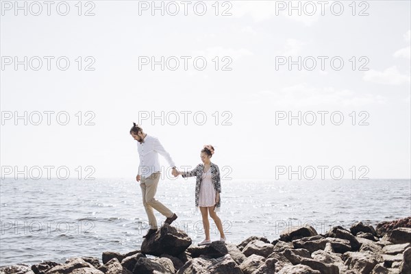 Middle Eastern couple walking on rocks near ocean