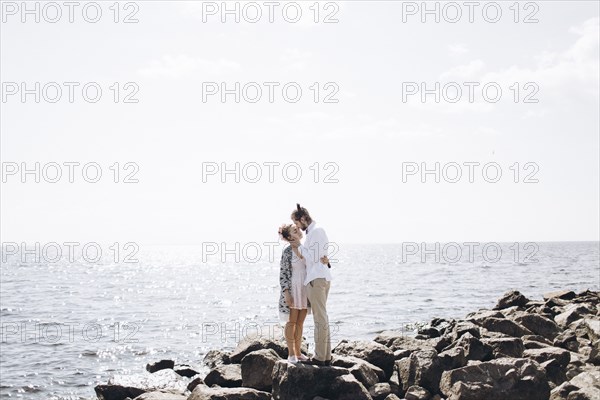 Middle Eastern couple hugging on rocks near ocean