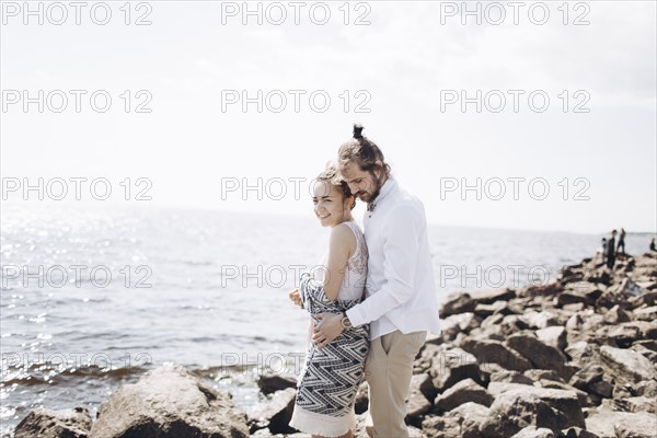 Middle Eastern couple hugging on rocks near ocean