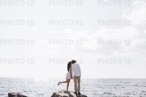 Middle Eastern couple kissing on rocks near ocean