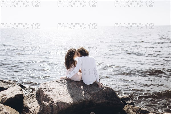 Middle Eastern couple sitting on rocks near ocean