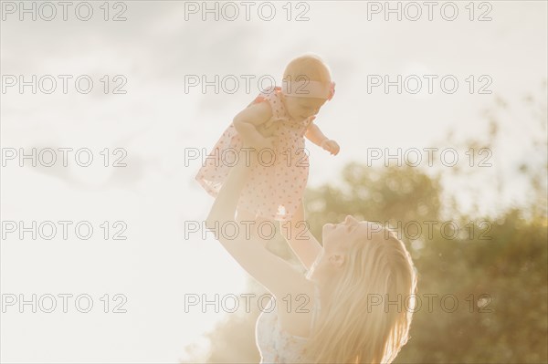 Mother lifting baby daughter on sunny day