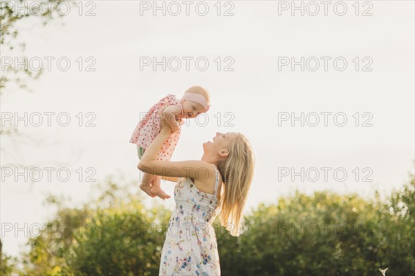 Mother lifting baby daughter on sunny day