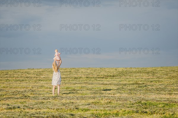 Mother lifting baby daughter in field