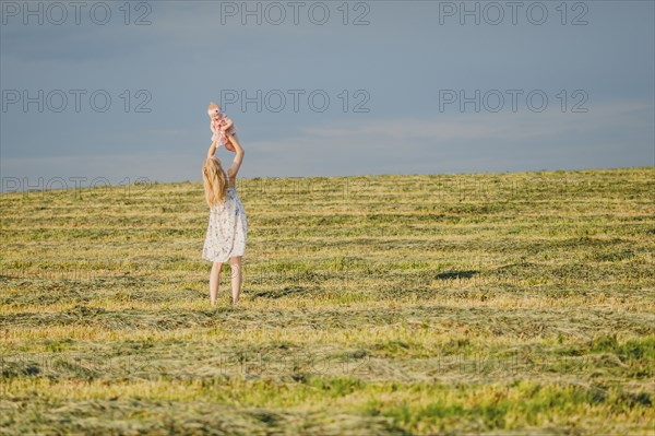 Mother lifting baby daughter in field