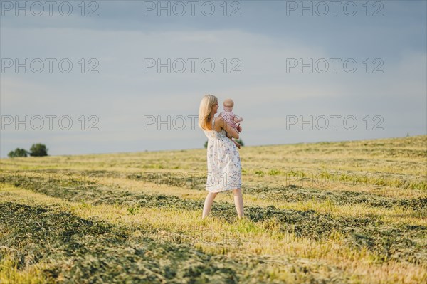 Mother carrying baby daughter in field