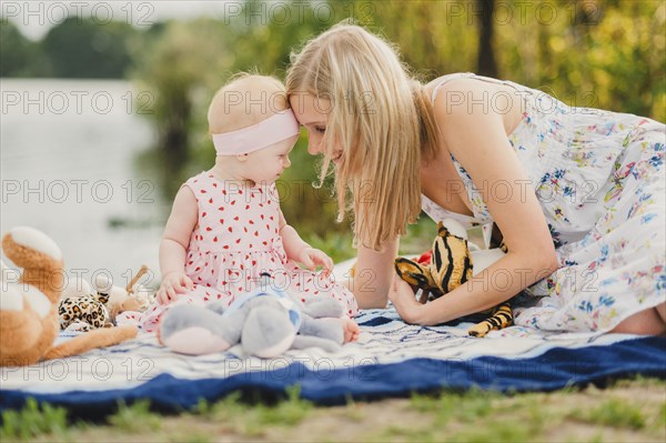 Mother and daughter playing with stuffed animals on blanket near lake