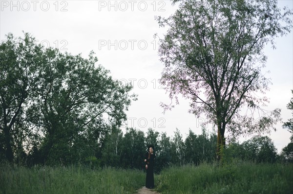 Middle Eastern woman wearing black dress on path in woods