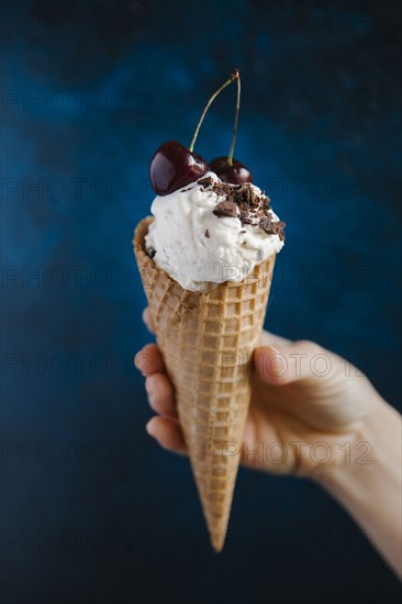 Hand holding ice cream cone with cherries