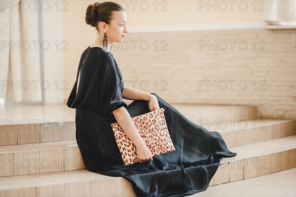 Glamorous Middle Eastern woman sitting on staircase holding purse