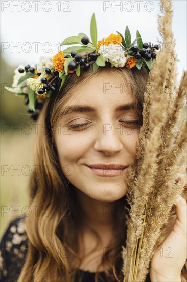 Middle Eastern woman wearing flower crown holding wheat to face