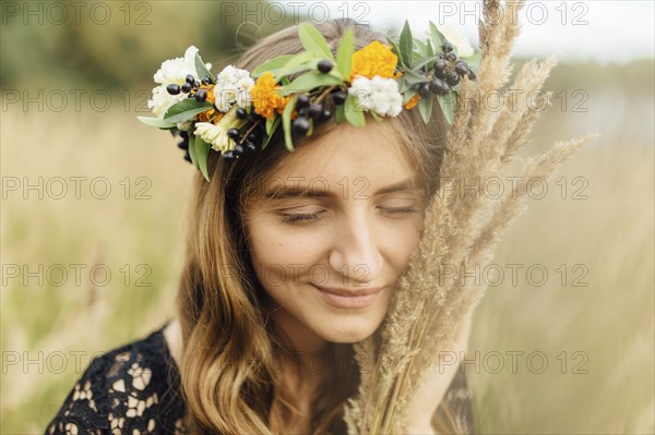 Middle Eastern woman wearing flower crown holding wheat to face