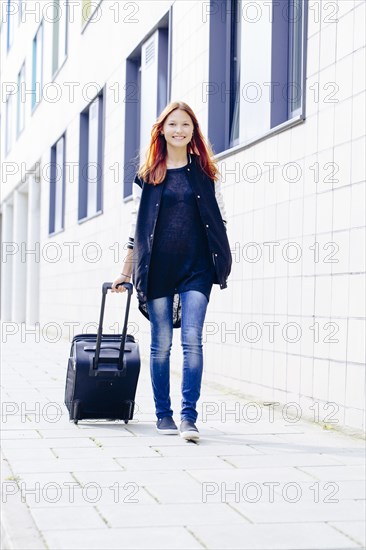 Mixed race woman rolling luggage