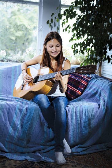 Mixed race woman playing guitar on sofa