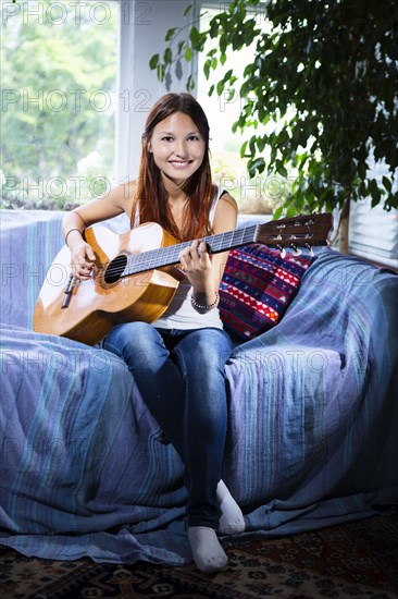 Mixed race woman playing guitar on sofa