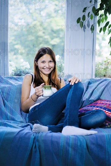 Mixed race woman drinking coffee on sofa