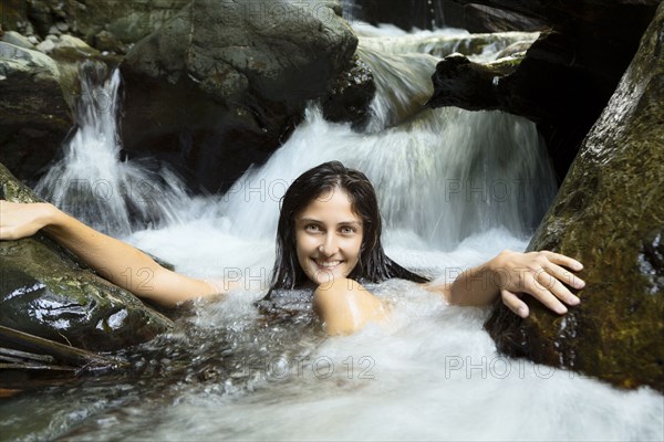 Mixed race woman sitting in waterfall