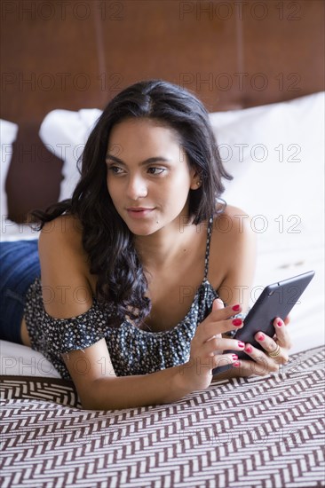 Hispanic woman using digital tablet on bed