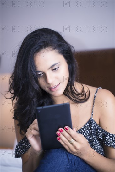 Hispanic woman riding digital tablet on bed