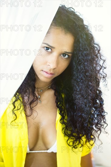 Mixed race woman peering behind curtain