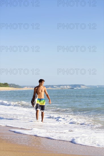 Mixed race surfer carrying surfboard on beach