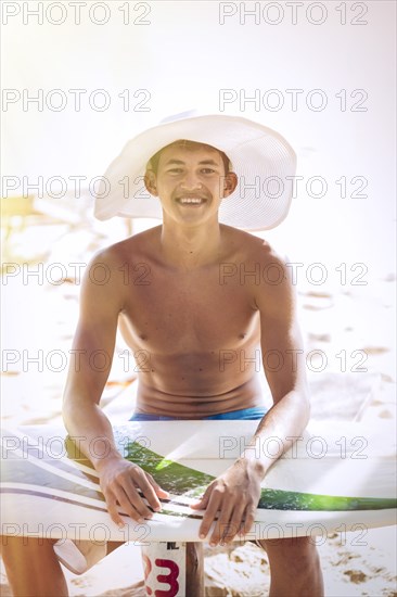 Mixed race teenage boy waxing surfboard on beach