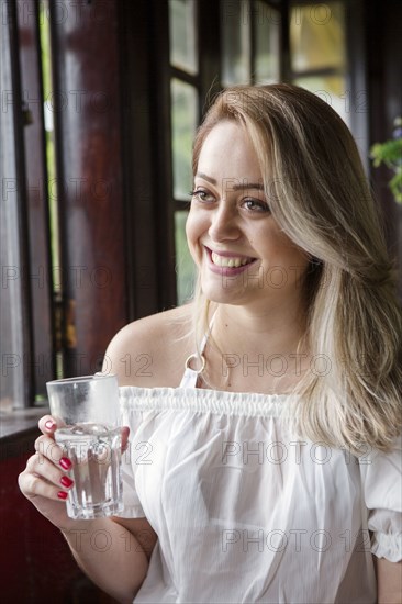 Smiling Hispanic woman drinking glass of water near window