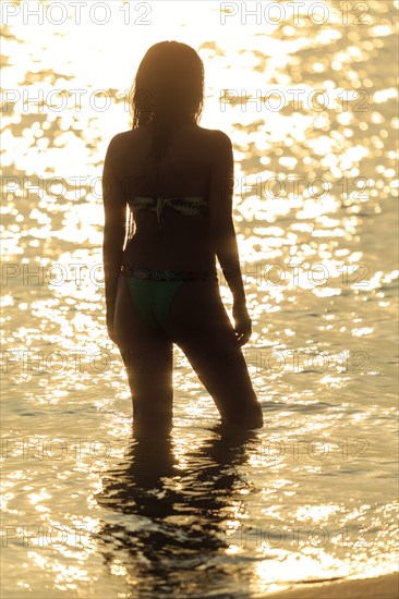 Silhouette of Mixed Race woman wading in ocean at sunset