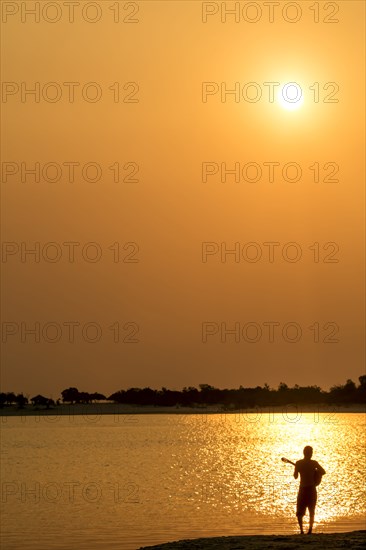 Silhouette of Caucasian man playing guitar at beach at sunset