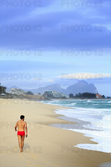 Hispanic man walking on beach near waves