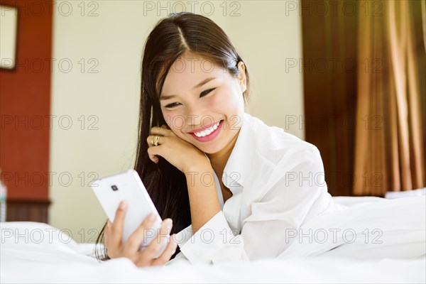 Smiling Asian teenage girl texting on cell phone