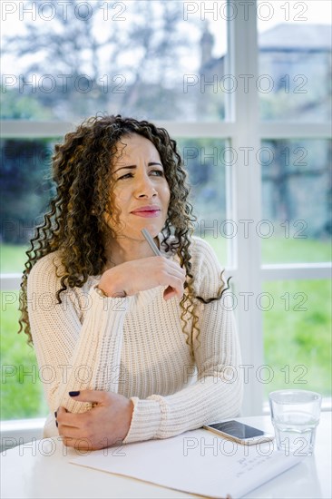 Curious woman sitting at table with pen and notepad