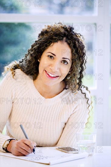 Smiling woman sitting at table writing on notepad with pen