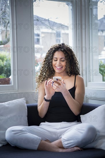 Smiling woman sitting near window texting on cell phone