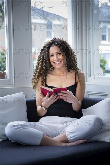 Smiling woman sitting near window reading book