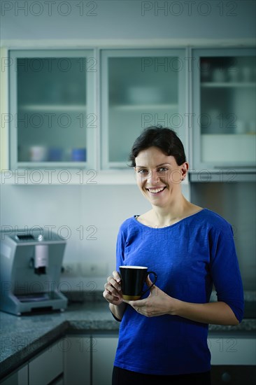 Smiling Caucasian woman drinking coffee in kitchen